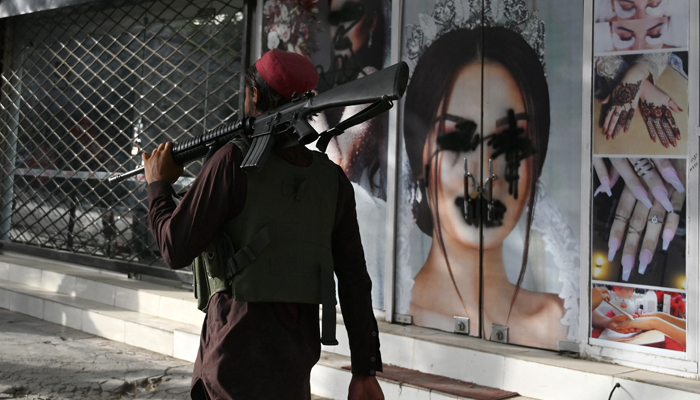 A Taliban fighter walks past a beauty saloon with images of women defaced using a spray paint in Shar-e-Naw in Kabul on August 18, 2021. &mdash; AFP/File