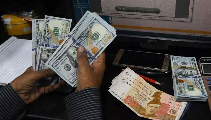 A currency dealer is counting notes of $100 while Rs5,000 notes are placed on the table. &mdash; AFP/File
