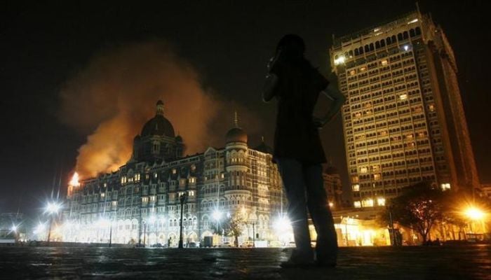 A reporter talks on her phone as smoke is seen coming from Taj Hotel in Mumbai, November 27, 2008 &mdash; Reuters