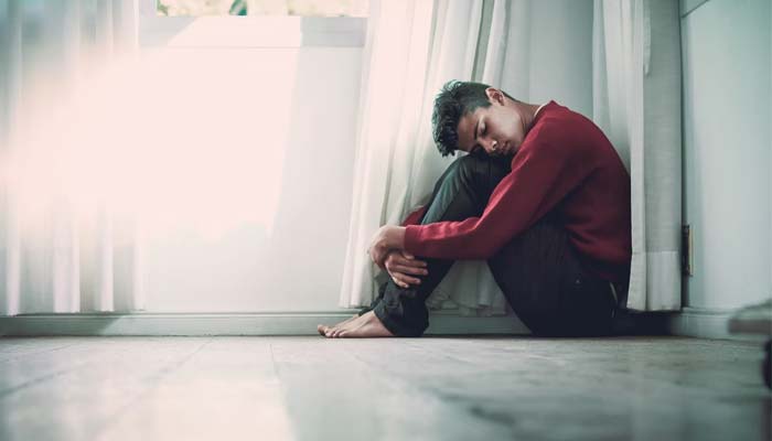 A boy sitting on the floor while he wraps his hands around his legs.&mdash; Unsplash