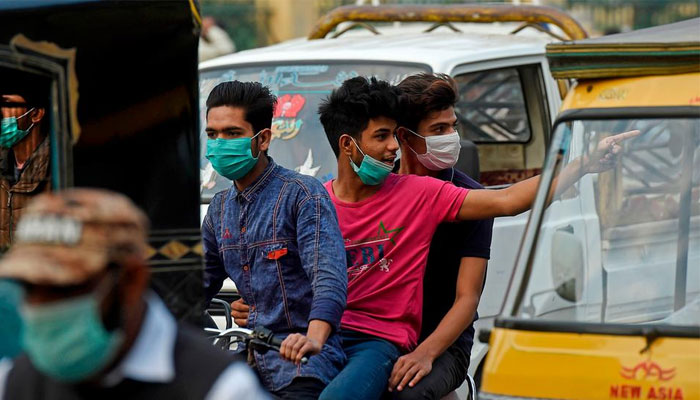 Three youngsters wearing masks ride a motorcycle on a busy thoroughfare in Pakistan. — AFP/File