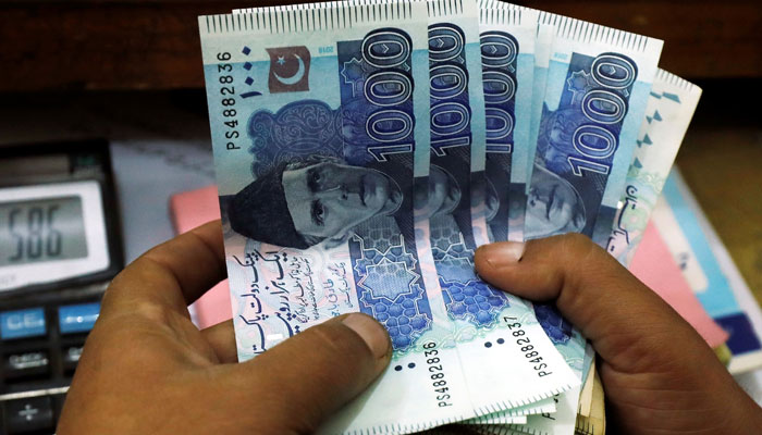 A trader counts rupee notes at a currency exchange booth in Pakistan in this undated photo. &mdash; Reuters/File