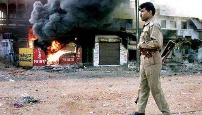 An Indian policeman stands on a street in Gujarat where shops can bee seen burnt releasing flames and smoke during the anti-Muslim riots in the state. &mdash; AFP/File