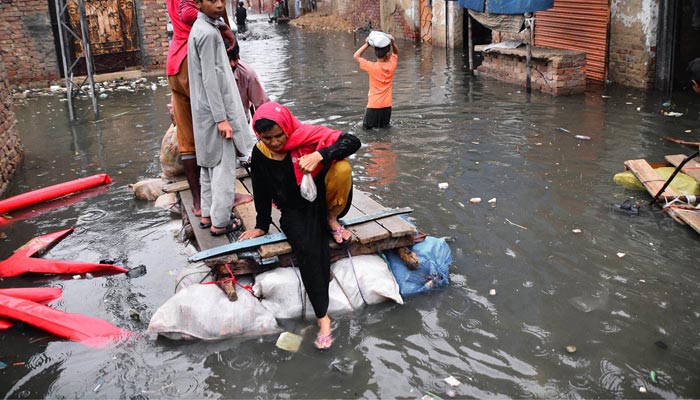 Rain affected people passing through rainwater on hand made boats after heavy rain in the city at Jinnah colony Latif Abad. &mdash; APP/File