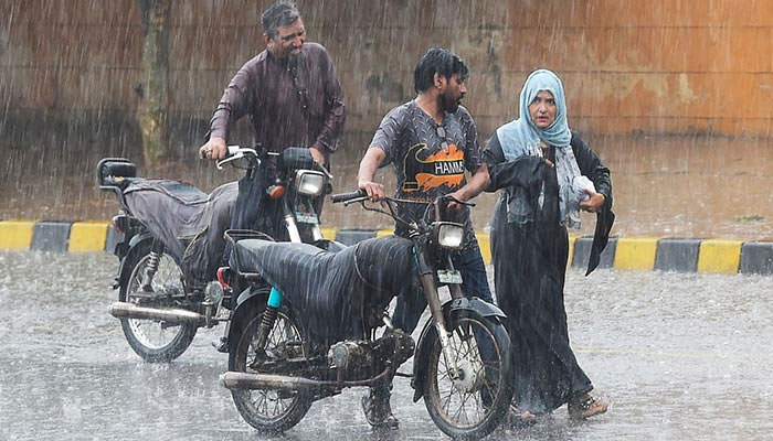 Commuters push their motorbikes along a street during a monsoon rainfall in Karachi on July 5, 2022. &mdash; AFP/File