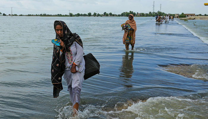 Displaced women wade through a flooded area after heavy monsoon rainfall in Rajanpur district of Punjab province on August 25, 2022. &mdash; AFP