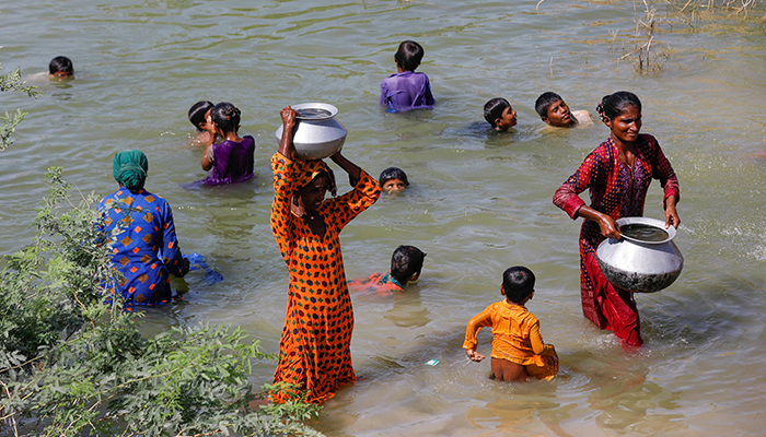 Displaced women carry water pots as children take bath amid floodwater, while they take refuge in a camp, following rains and floods during the monsoon season in Sehwan, Pakistan, September 16, 2022. — Reuters