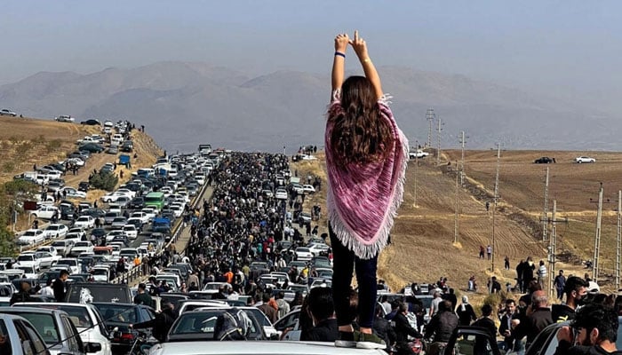 This UGC image posted on Twitter on 26 October 2022 shows an unveiled woman atop a vehicle as thousands of people make their way to the Aichi cemetery in Saqez, Mahsa Aminis hometown. — AFP/File