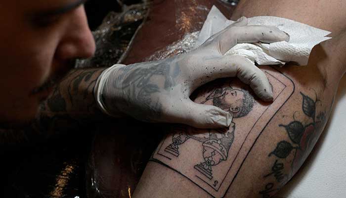 Argentine tattooist Tebi Cobra Vucinovich works on a tattoo of Argentina´s forward Lionel Messi kissing the FIFA World Cup trophy on the leg of Ariel Sacchi at Ds Tattoo Shop in Buenos Aires on December 23, 2022. — AFP