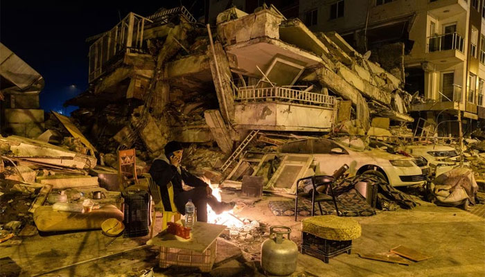 A man speaks on the phone as he sits by a fire near a destroyed building in the aftermath of a deadly earthquake in Antakya, Turkey February 20, 2023. — Reuters