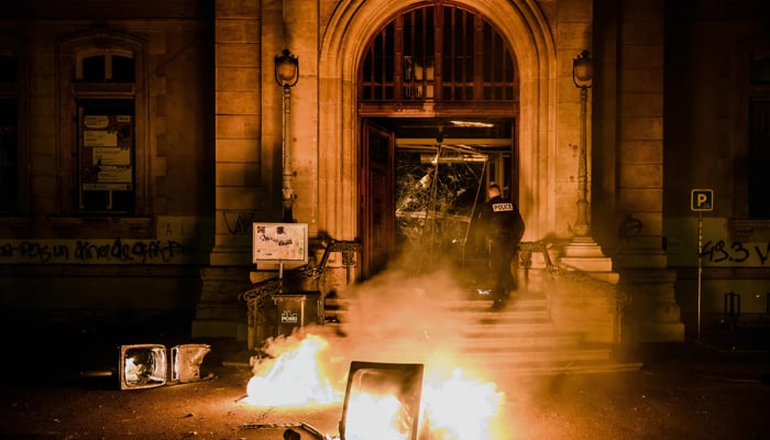 A police officer attempts to extinguish flames at the entrance of the town hall of the 4th arrondissement (district) of Lyon which was vandalised during riots following a demonstration on March 17, 2023 in Lyon,. — AFP