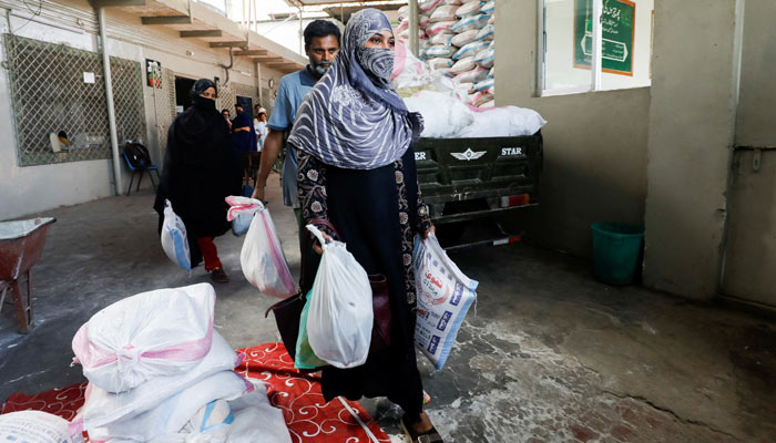 People walk with charity ration sacks received from the Saylani Welfare Trusts office, a non-government organisation focusing primarily on feeding the poor and homeless, in Karachi on April 3, 2023. — Reuters