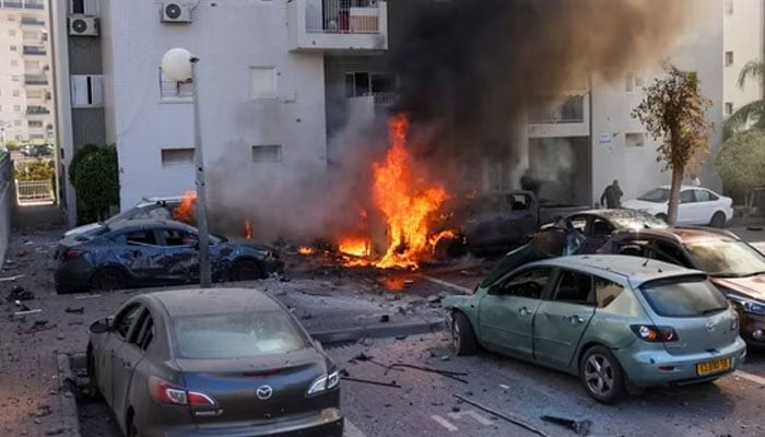 A member of the Israeli security forces stands near burning cars following a rocket attack from the Gaza Strip in Ashkelon, southern Israel, on October 7, 2023. — AFP
