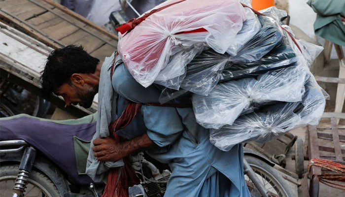 A labourer bends over as he carries packs of textile fabric on his back to deliver to a nearby shop in a market in Karachi, Pakistan June 24, 2022. — Reuters