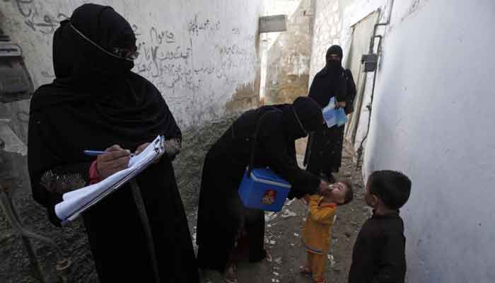 A polio vaccinator (2nd L) administers polio vaccine drops to a boy while a colleague takes notes nearby, along a street in a Karachi slum on October 20, 2014. — Reuters