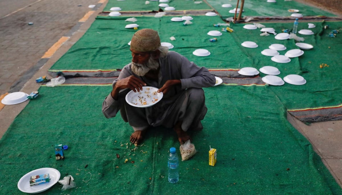 A man sits with empty plates as he eats boiled rice after breaking his fast at an event organised by a charity organisation during Ramadan, along a sidewalk in Karachi. — Reuters/File