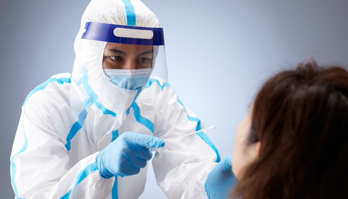 A doctor dressed in a hazmat suit checks their patient for COVID-19. — Canva