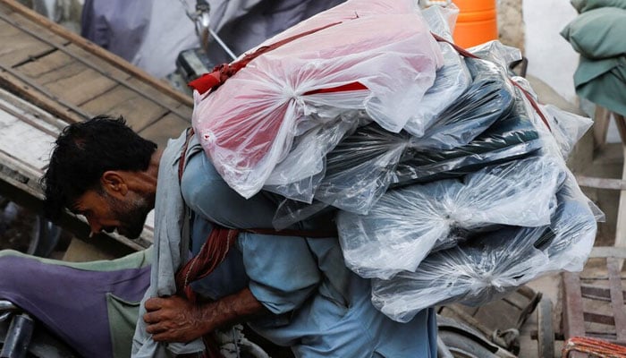 A labourer bends over as he carries packs of textile fabric on his back to deliver to a nearby shop in a market in Karachi. — Reuters/File