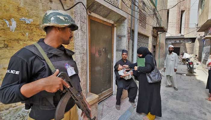 A Pakistani policeman stands guard as a health worker administers polio drops to a child during a polio vaccination campaign in Peshawar, Pakistan, on September 14, 2015. — AFP/File
