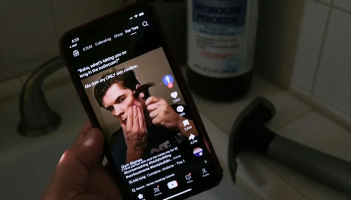 A person holds a cellphone showing a person using hammer to chisel his jawline as part of lookxmaxxing trend. — AFP/File