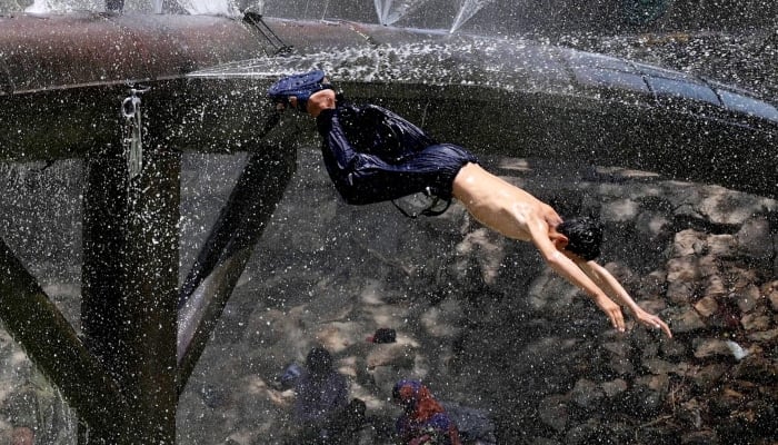 A Youngster enjoys diving for bathing from a leaking water supply line over the water canal during hot weather in Hyderabad, April 28, 2025. — APP