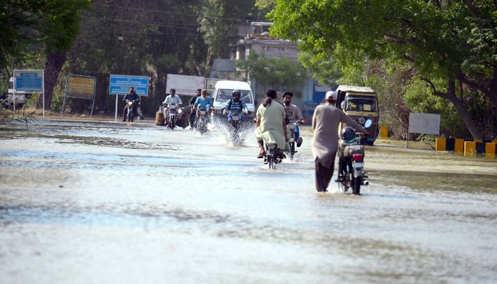 Commuters are passing through an inundated road by overflowing drinking water after bursting drinking water lines, located at Karachi University residential premises in Karachi on Tuesday, April 29, 2025. — APP