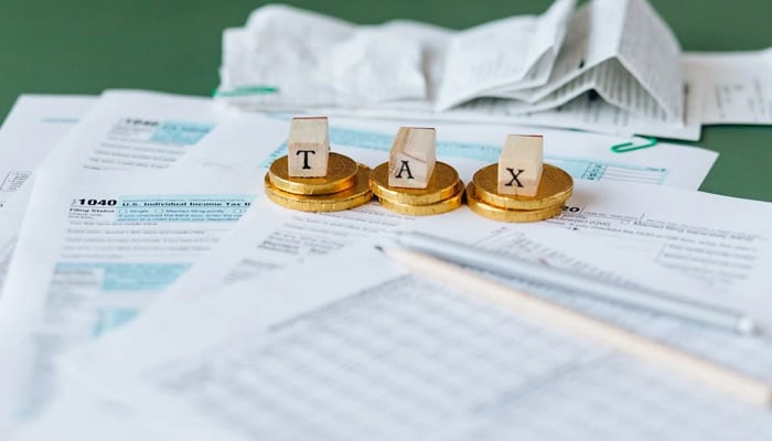 A representational image of a table where coins and cubes with tax letters written on them are placed on the papers. — Pexels