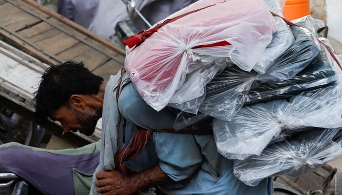 A labourer bends over as he carries packs of textile fabric on his back to deliver to a nearby shop in a market in Karachi. — Reuters/File