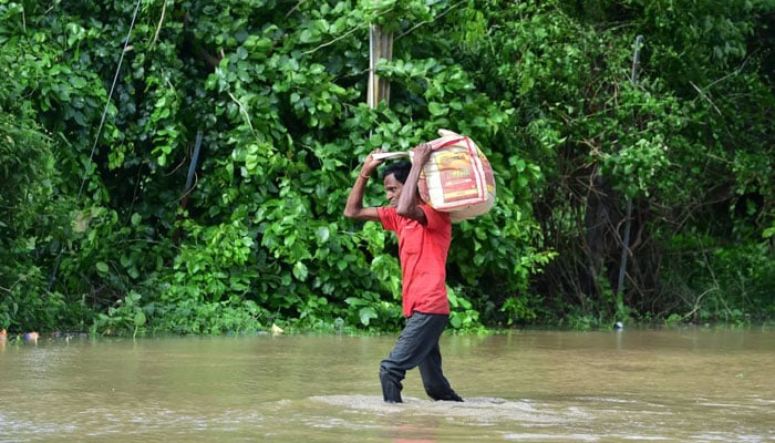 A man carries his belongings through a flooded street after heavy rains on the outskirts of Ahmedabad, India. — AFP/File