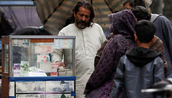 A currency broker stands near his booth, which is decorated with pictures of currency notes, while dealing with customers, along a road in Karachi, January 27, 2023. — Reuters