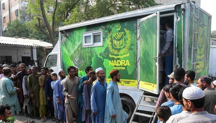 Afghan refugees queue outside a National Database and Registration Authority (NADRA) vehicle at a Karachi police station to have their data verified On November 8, 2023. — AFP