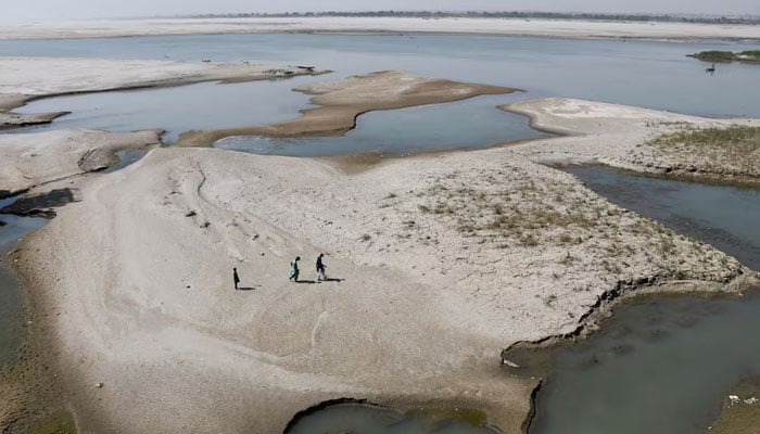 People walk on the dry patch of the Indus River, in Jamshoro, on March 15, 2025. — Reuters