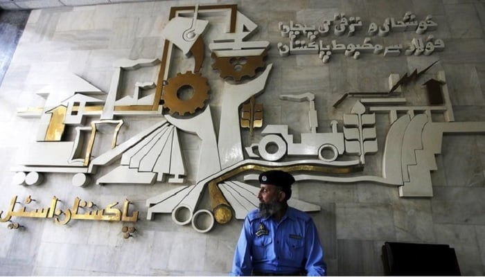 A security guard sits in front of a wall with signs and slogans at the operation building at the Pakistan Steel Mills on the outskirts of Karachi.—Reuters/File