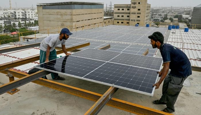 In this photograph taken on July 2, 2025, technicians install solar panels on the rooftop of a factory in Karachi. — AFP