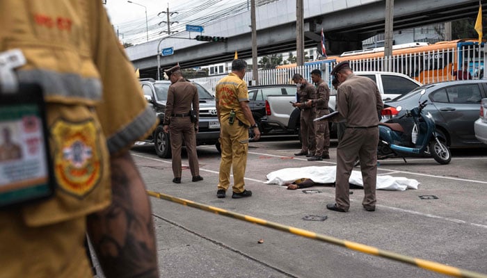 Thai police stand next to a covered body as they inspect the scene after four security guards were killed in a shooting at Or Tor Kor Market in Bangkok on July 28, 2025. — AFP