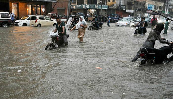 People wade through a flooded street after heavy rainfall in Karachi on August 19, 2025. — AFP