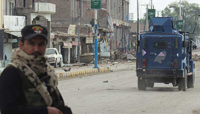 A police officer stands guard on a street with damaged shops in the background, following a militant attack on the FC headquarters in Bannu, Khyber Pakhtunkhwa on September 2, 2025.
