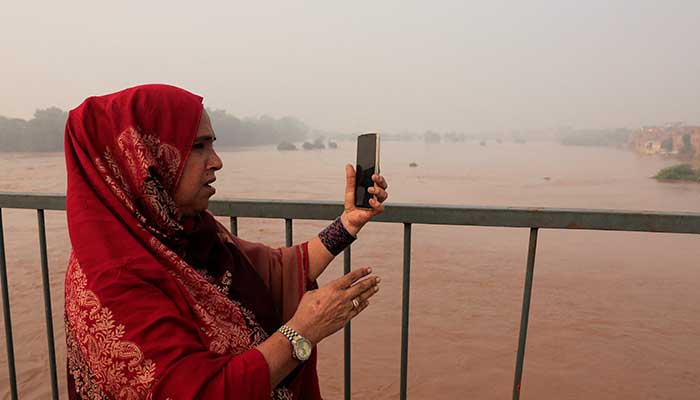 A woman records a video at she stands on Ravi bridge, following the monsoon rains and rising water level of the Ravi River in Lahore on August 29, 2025. — Reuters