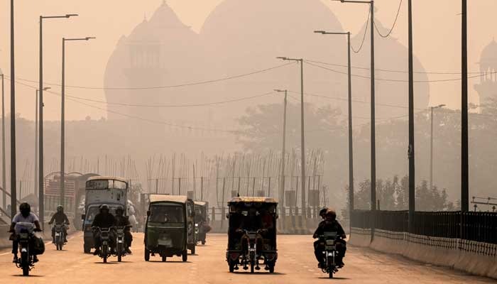 Commuters ride along a street engulfed in smog, in Lahore on November 5, 2024. — AFP