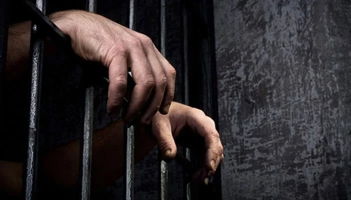Representational image of a handcuffed man standing behind the bars. — AFP