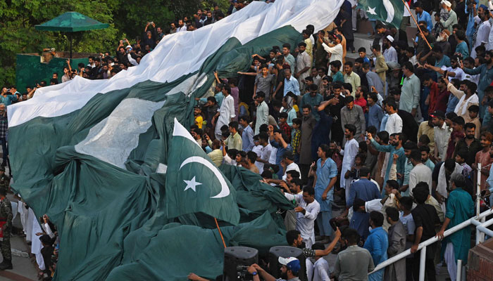 People carry a giant Pakistani flag while watching ´Beating the Retreat´ ceremony on the eve of the countrys Independence Day celebrations at the Pakistan-India Wagah border post, about 35km from Lahore on August 13, 2023.  — AFP