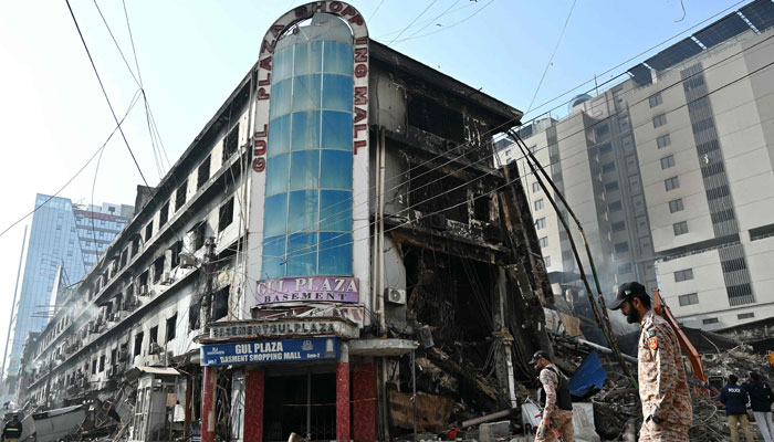 Sindh Rangers personnel walk past by charred remains of a Gul Plaza shopping mall in Karachi on January 22, 2026. — AFP
