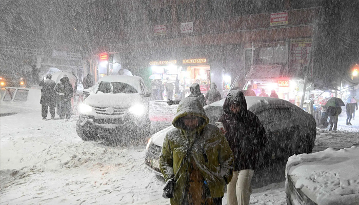 Tourists walk along a road as it snows heavily in Murree on January 23, 2026. — AFP