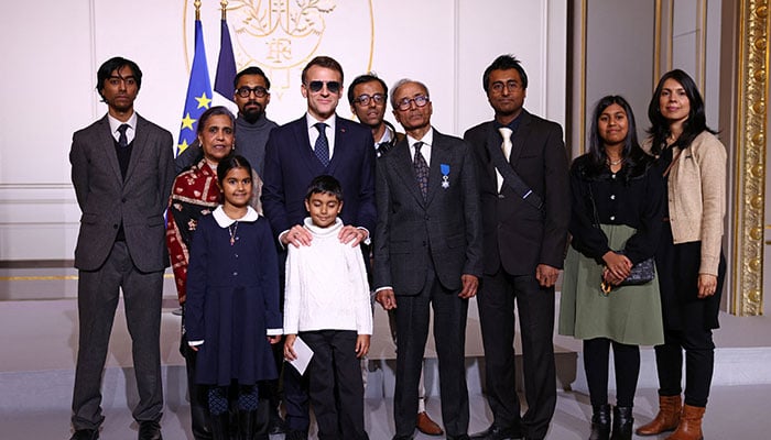 French President Emmanuel Macron poses with Ali Akbar, who hawks newspapers around the streets of Saint-Germain-des-Pres in the French capital for 50 years, awarded with the Chevalier of the French Order of Merit award and his family during a ceremony at the Elysee Palace in Paris, France on January 28, 2026. — Reuters