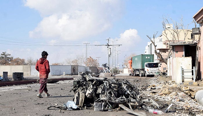 A person walks past the remains of a damaged vehicle at a site, after militant attacks, in Quetta on February 1, 2026. — Reuters