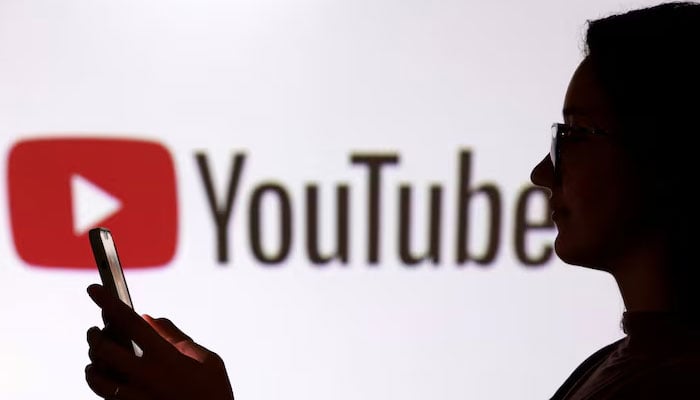 A teenager poses for a photo while holding a smartphone in front of a Youtube logo in this illustration taken on September 11, 2025. — Reuters