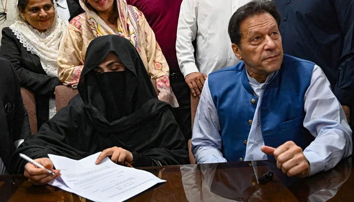 Former prime minister Imran Khan (right) along with his wife Bushra Bibi signs surety bonds for bail in various cases, at the registrars office in the Lahore High Court on July 17, 2023. — AFP