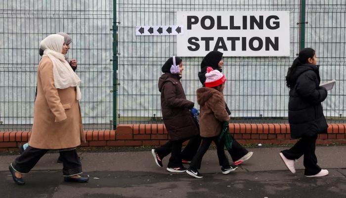 Women and children walk past a signage outside a polling station at St Agnes Primary School, on the day of the Gorton and Denton by-election, triggered by the resignation of Andrew Gwynne, in Gorton, Manchester, Britain, February 26, 2026. — Reuters
