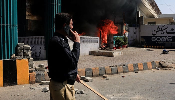 A police officer walks next to a checkpost set ablaze in a protest outside the S Consulate General, following news of US and Israeli strikes on Iran that martyred supreme leader Ayatollah Ali Khamenei, in Karachi on  March 1, 2026. — Reuters