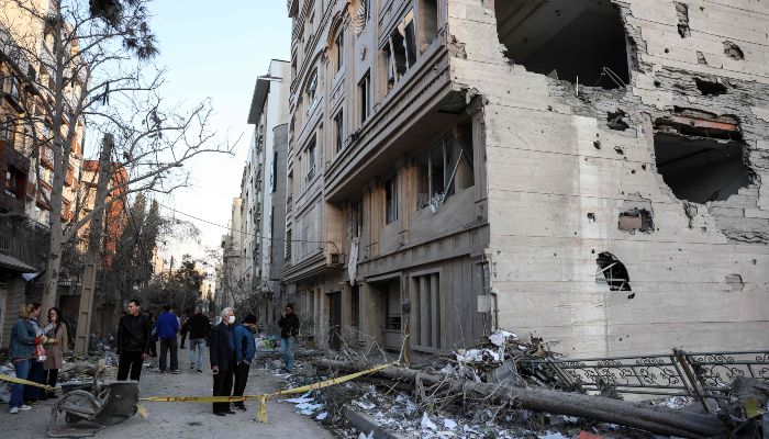 Residents stand on a street beside damaged residential buildings near Niloufar square in Tehran during the ongoing joint US-Israeli military campaign on Iran on March 2, 2026.